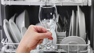 Mão a retirar copo de pé de vidro de dentro da máquina de lavar loiça.